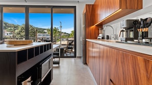 A modern kitchen with wooden cabinets, a large island, and a view of a balcony with a cityscape and greenery. - Casa Formosa · Modern 2BR + Rooftop Pool (Puerto Vallarta)