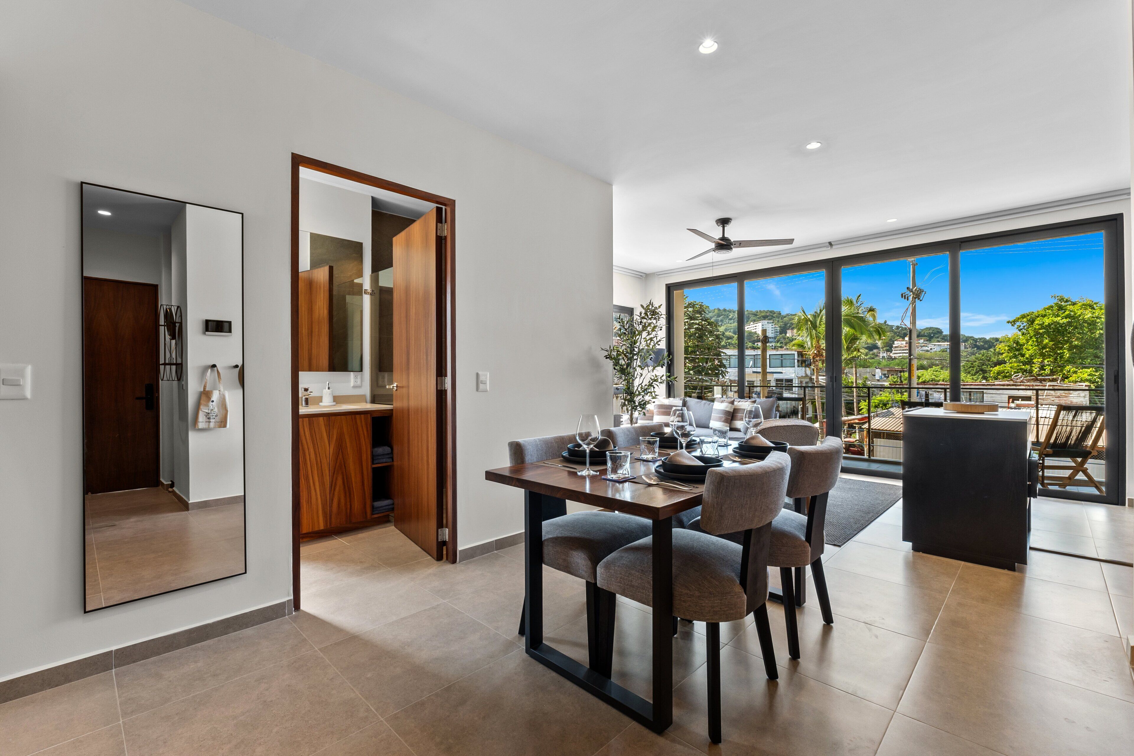 A modern dining area with a large table, chairs, and a view of the outdoors through large windows.