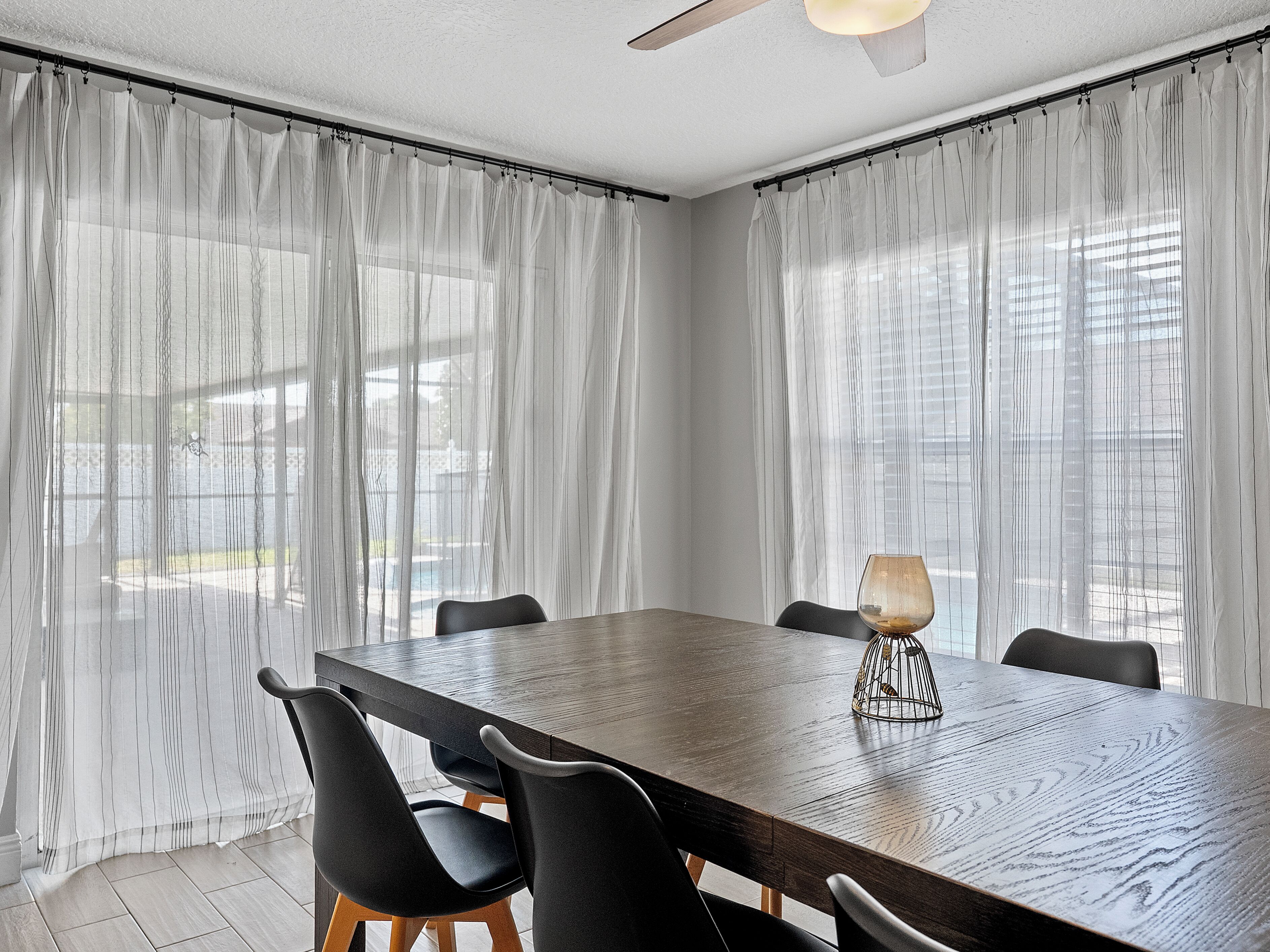 A dining area with a large wooden table, black chairs, and sheer curtains.