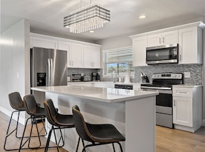A modern kitchen with white cabinets, a stainless steel refrigerator, a microwave, and a large island with bar stools.