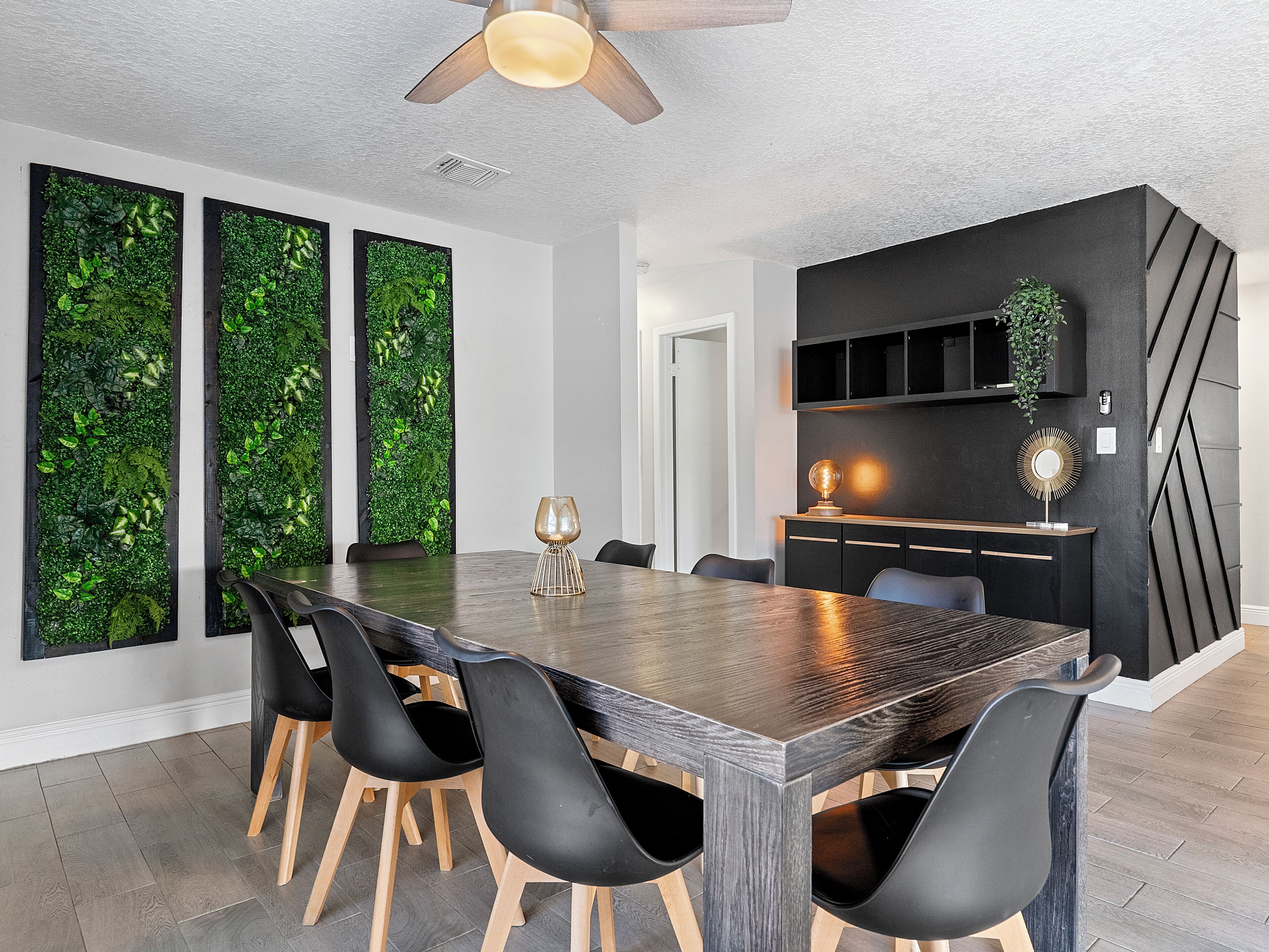 A modern dining area with a wooden table, black chairs, and a ceiling fan.