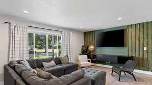 En moderne stue med en modulsofa, et fladskærms-tv monteret på en grøn væg og et stort vindue med gardiner.