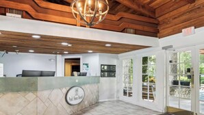 The front entrance to Park Shore Resort with a reception desk, a chandelier, and a sign indicating an exit. - Beautiful Updates - Relaxing Views - Close to Pool (Naples)