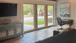A spacious living room with a large window, a sofa, a TV, and a desk with a chair. - Beautiful Updates - Relaxing Views - Close to Pool (Naples)