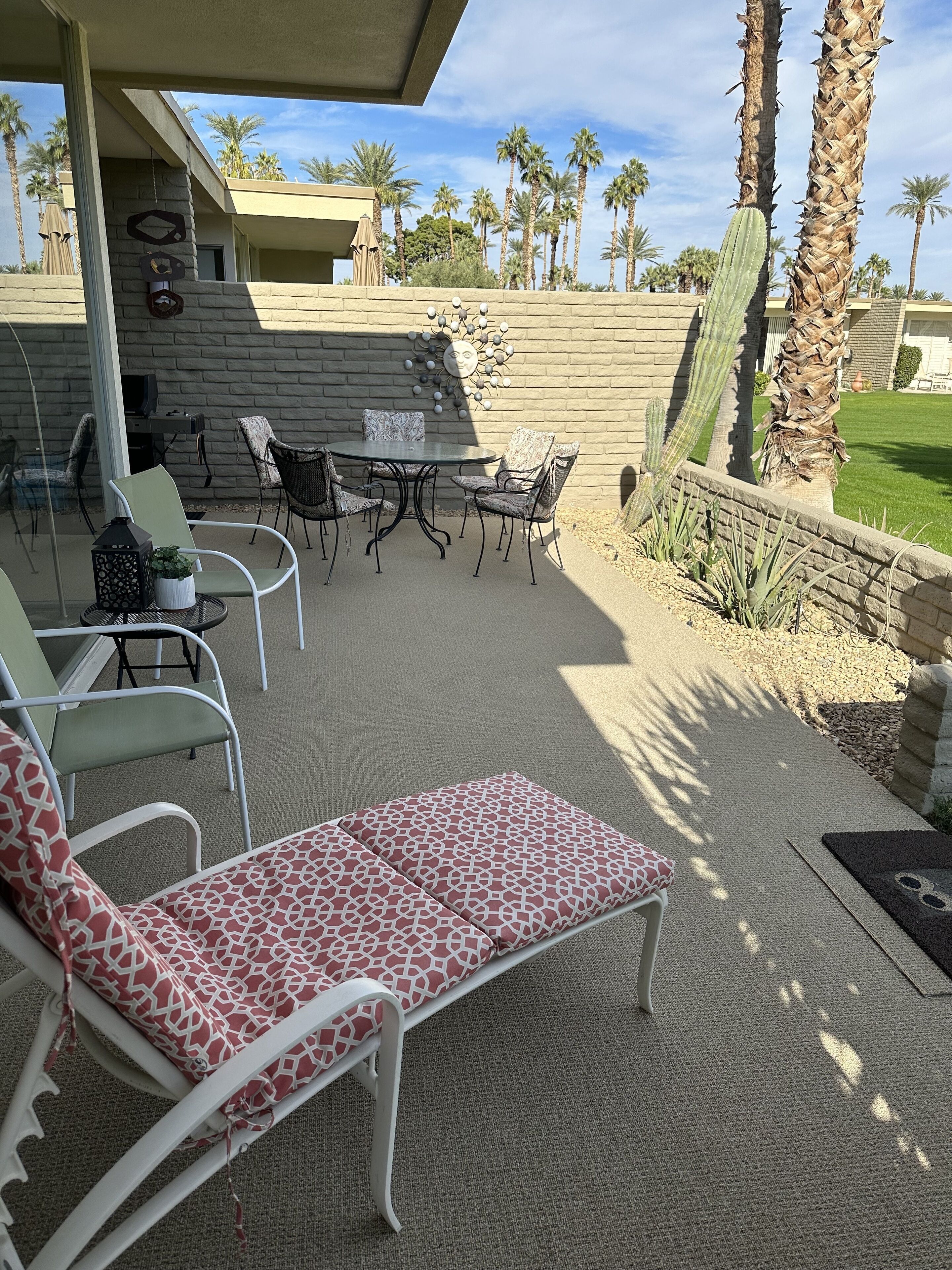 Un espace extérieur aménagé en terrasse, avec une table et des chaises, un fauteuil confortable et un cactus.