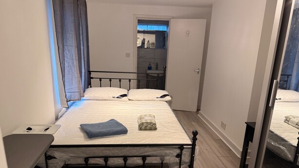 Une petite chambre bien éclairée, avec un lit simple, une table de chevet et un miroir.