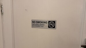 Une porte blanche portant un panneau « Il est interdit de fumer », y compris les cigarettes électroniques et les dispositifs de vapotage.