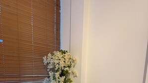 Un coin repas avec une table blanche, des chaises noires, un arrangement floral et une fenêtre avec des stores.