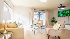 Un salon moderne avec une table basse en verre, des canapés de couleur beige et un téléviseur fixé au mur.