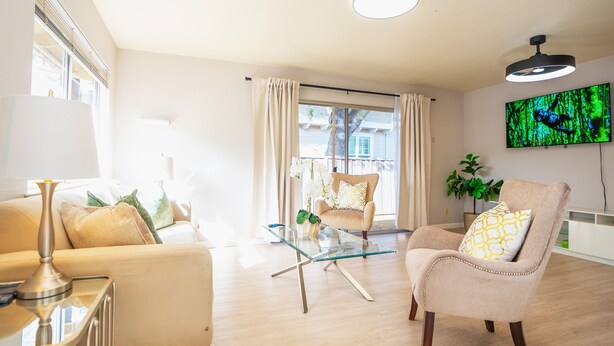 Una sala de estar moderna con una mesa de centro de vidrio, sofás color beige y un televisor montado en la pared.