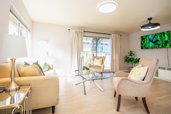 A modern living room with a glass coffee table, beige sofas, and a television mounted on the wall. - Spacious Mountain View DT 3BR Gem Great for Work & Family (Mountain View)