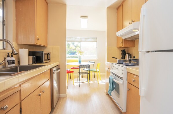 A compact kitchen with wooden cabinets, a sink, a microwave, a stove, and a dining area with a table and chairs. - Spacious Mountain View DT 3BR Gem Great for Work & Family (Mountain View)