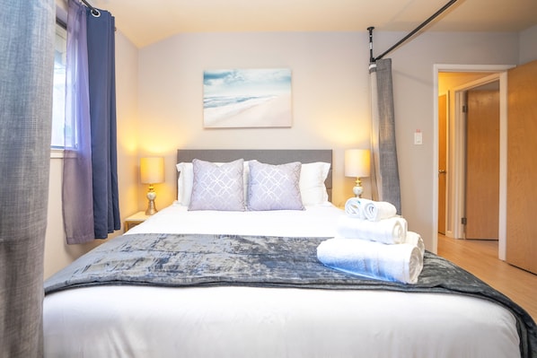 Een net opgemaakt bed met een geborduurde deken, twee kussens en een opgevouwen handdoek aan de zijkant.