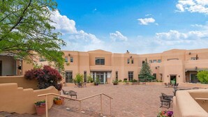 A courtyard with a brick floor, outdoor seating, and a building with multiple windows and doors. - Quail Run 101 | Private Patio | Golf Course | Pool & Hot Tub | Tennis & Pickleball | Spa (Santa Fe)