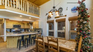 A spacious kitchen with a central island, wooden chairs, and a dining table. A decorated Christmas tree is visible in the background. - Bearfoot Lodge in Angel Fire (Angel Fire)