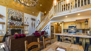 A cozy living room with a fireplace, a dining area with wooden furniture, and a kitchen with modern appliances. - Bearfoot Lodge in Angel Fire (Angel Fire)