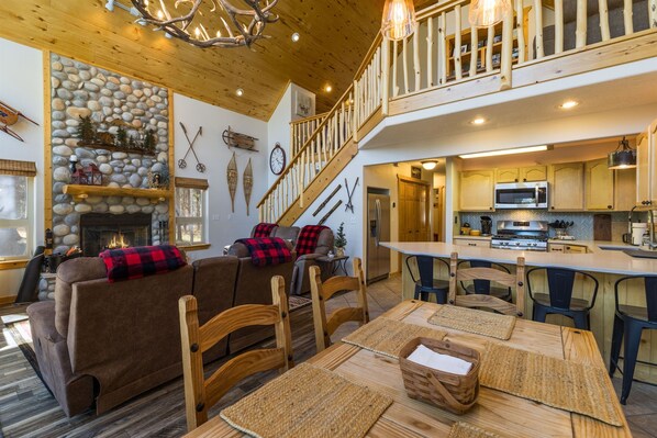 A cozy living room with a fireplace, a dining area with wooden furniture, and a kitchen with modern appliances. - Bearfoot Lodge in Angel Fire (Angel Fire)