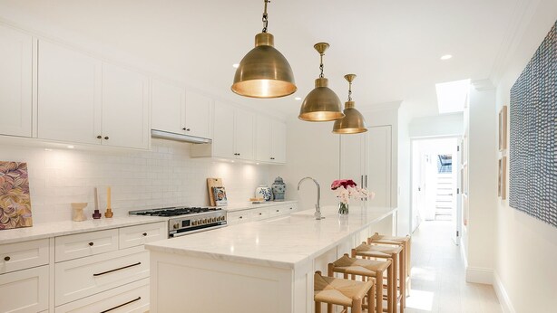 Una cocina moderna con armarios blancos, una isla central con taburetes de bar e iluminación colgante.
