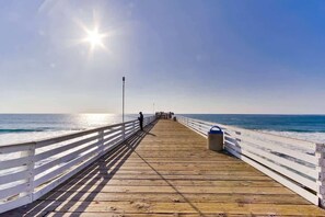 Une jetée en bois s’étendant dans l’océan, sous un ciel dégagé et un soleil éclatant.
