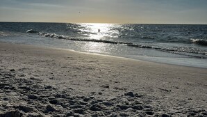 A beach with a clear sky, sun reflecting off the water, and footprints in the sand. - Cozy Barefoot Beach Condo E-217 – Just 100 Steps from Indian Shores Beach. (Indian Shores)