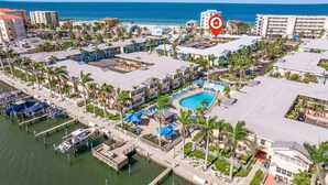 An aerial view of a coastal hotel with a swimming pool, multiple buildings, and a marina. - Cozy Barefoot Beach Condo E-217 – Just 100 Steps from Indian Shores Beach. (Indian Shores)