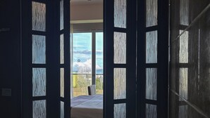 Ein Badezimmer mit Badewanne, einem Fenster mit Blick auf Himmel und Wolken sowie einer Tür mit vertikalen Jalousien.