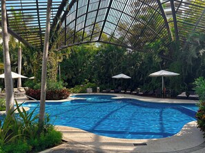 Ein Swimmingpool mit Liegestühlen und Sonnenschirmen, umgeben von üppiger Vegetation.