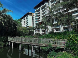 Ein Hotel mit mehreren Etagen, einer Holzbrücke über dem Wasser und üppiger Vegetation.