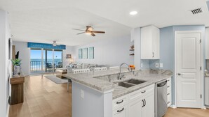 A modern kitchen with a central island, white cabinetry, and a view to the outside. - Luxurious Penthouse W/ Direct Ocean Front  Balcony, Heated Pool & Hot Tub!  🌊 (Cape Canaveral)