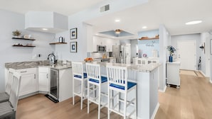 A modern kitchen with white cabinetry, a marble countertop, and bar stools. - Luxurious Penthouse W/ Direct Ocean Front  Balcony, Heated Pool & Hot Tub!  🌊 (Cape Canaveral)