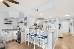 A modern kitchen with white cabinetry, a marble countertop, and bar stools. - Luxurious Penthouse W/ Direct Ocean Front  Balcony, Heated Pool & Hot Tub!  🌊 (Cape Canaveral)