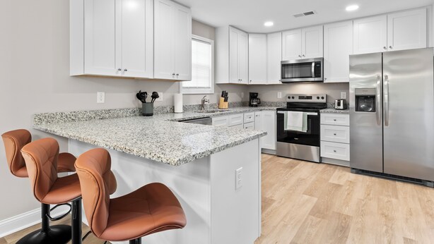 A modern kitchen with white cabinets, stainless steel appliances, granite countertops, and brown bar stools. - The Aspen ~ New, Trendy 3 Bed Near The Action (Kannapolis)