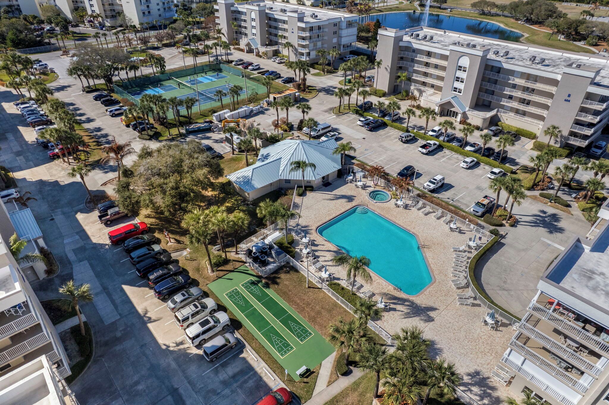 Vista aérea de un complejo hotelero con varias edificaciones, una piscina, canchas de tenis y un estacionamiento.