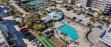 Vista aérea de un complejo hotelero con varias edificaciones, una piscina, canchas de tenis y un estacionamiento.