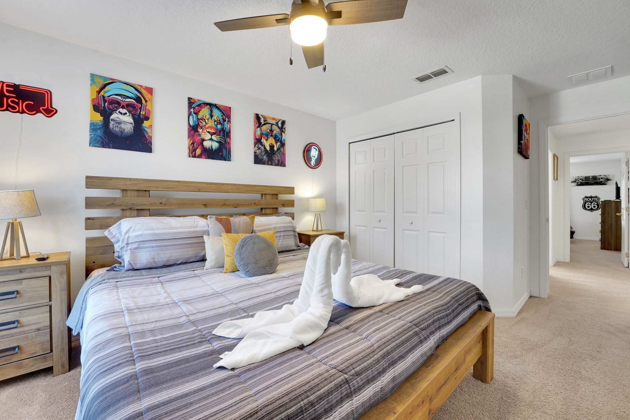 Un dormitorio con cama, cabecera de madera, decoración en la pared, ventilador de techo y puerta que da a otra habitación.