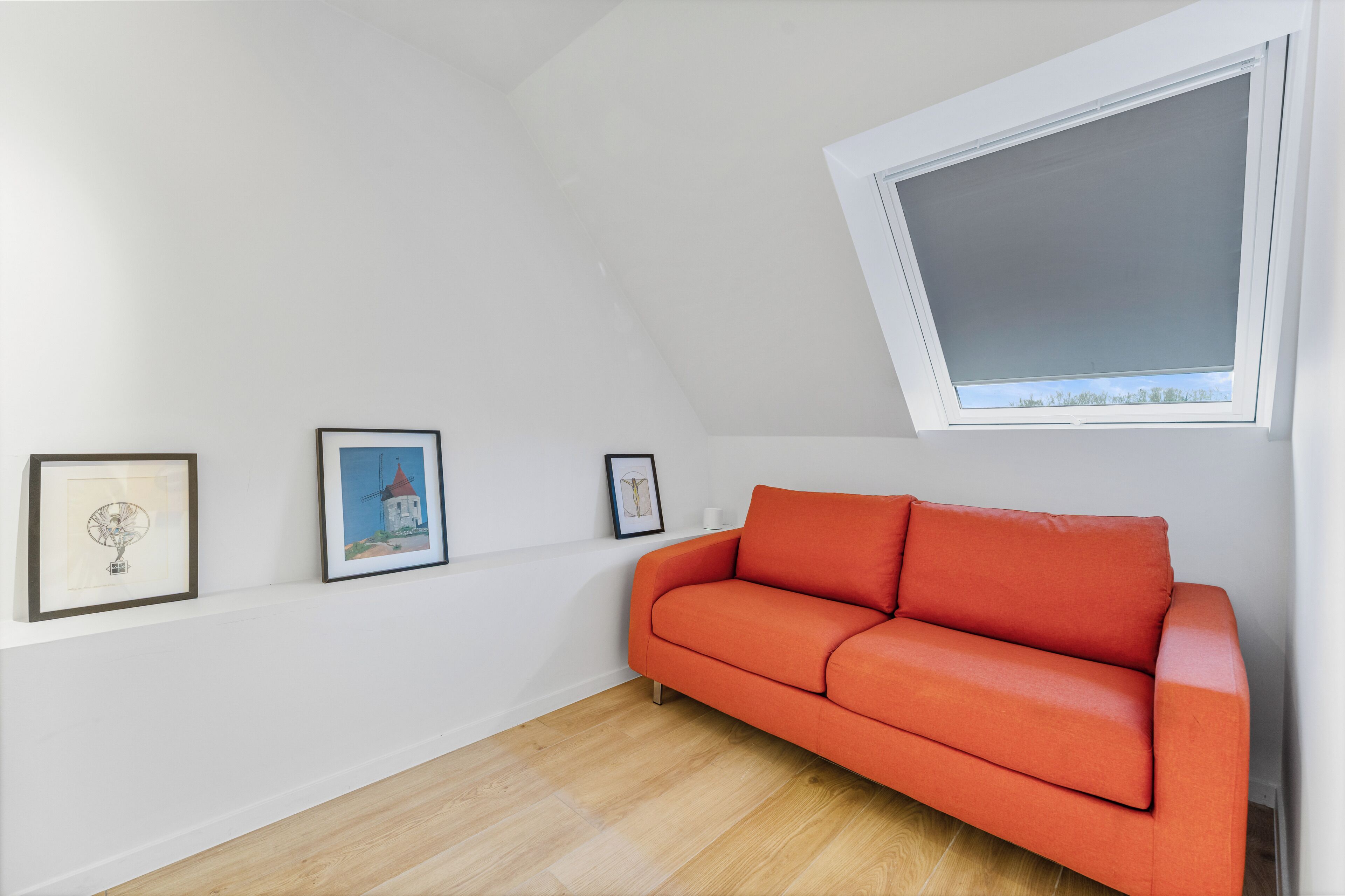 A room with a white wall, a wooden floor, a red sofa, and a window with a view.