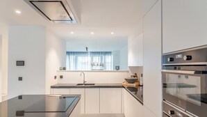 Een moderne keuken met witte kasten, een zwart aanrecht, een inbouwoven en een raam met gordijn.