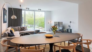 Een moderne woonkamer met een ronde eettafel, een bank en een groot raam met uitzicht op groen.