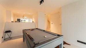 Een pooltafel in een moderne ruimte met een trap en een keuken in de achtergrond.