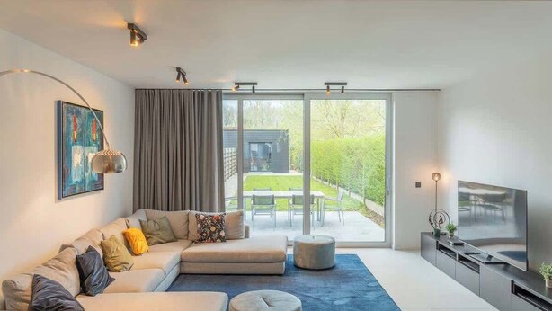 Een moderne woonkamer met een ruime hoekbank, een flatscreen televisie en een schuifpui naar een terras.