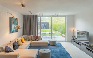 A modern living room with a large sectional sofa, a flat-screen TV, and a sliding glass door leading to an outdoor patio. - Modern & Spacious House (Kortrijk)