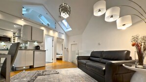 Ein moderner Wohnraum mit einer offenen Küchenzeile im Loft-Stil, einem schwarzen Ledersofa und einem großen Oberlicht.