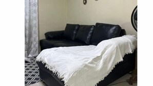 Ett rum med en svart soffa, en vit pläd och dekorativ väggkonst.