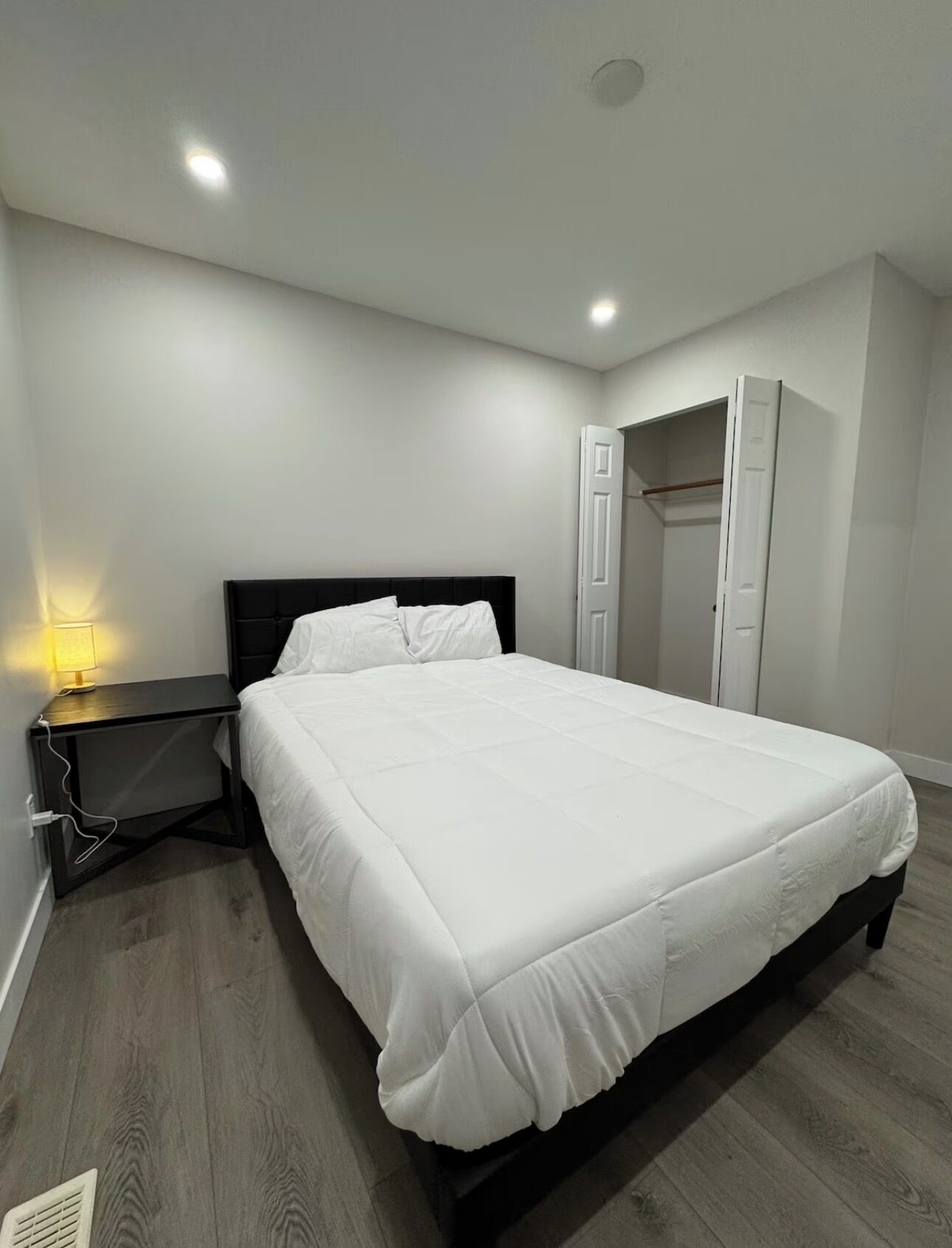 Un dormitorio moderno con una cama grande, una mesita de noche con lámpara y un armario.