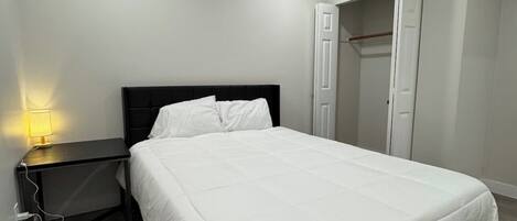 Un dormitorio moderno con una cama grande, una mesita de noche con lámpara y un armario.