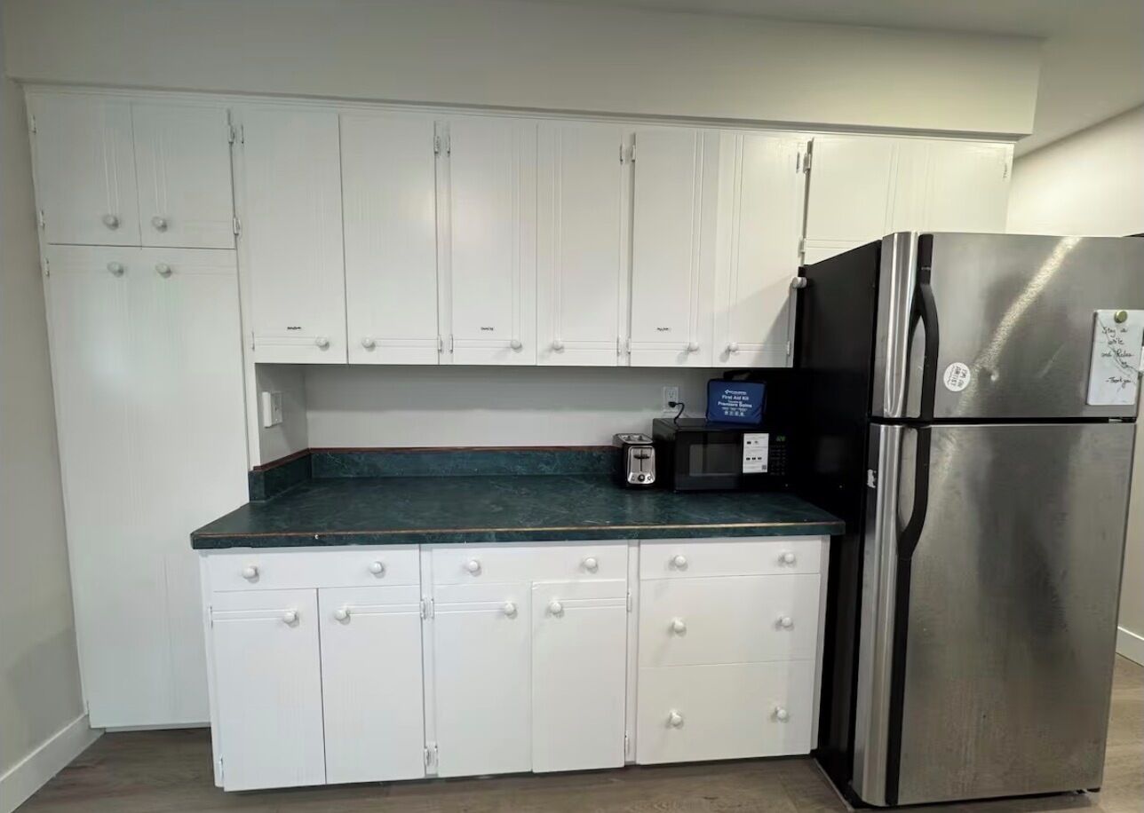 A kitchen with white cabinets, a stainless steel refrigerator, and a black countertop.