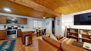 Uma sala de estar aconchegante com sofá de couro, área de jantar com mesa e cadeiras, cozinha com eletrodomésticos modernos e uma televisão de tela plana na parede.