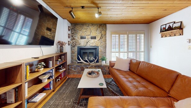 Uma sala de estar acolhedora com lareira de pedra, sofá de couro, estantes de madeira com livros e uma TV de tela plana.