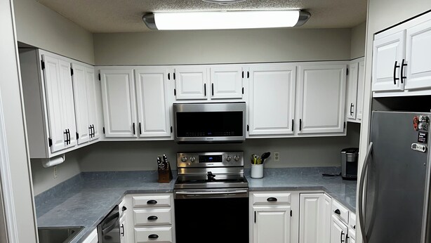A modern kitchen with white cabinets, stainless steel appliances, and a wooden floor.