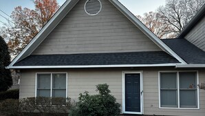 A single-story house with a gabled roof, a front door, and a small front yard with a bush.